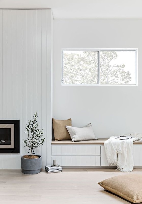 an airy nook with a built-in fireplace and a bench with drawers for storage plus pillows and a fringe blanket and a pitted plant