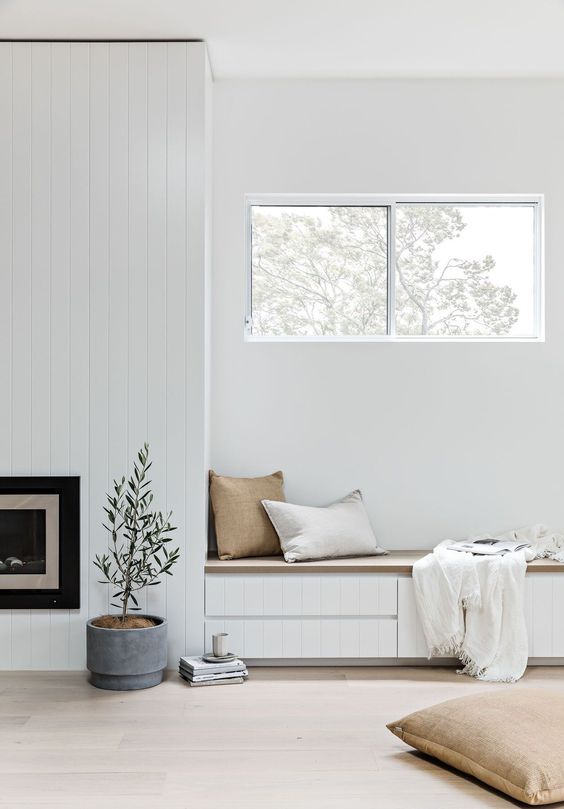 an airy nook with a built-in fireplace and a bench with drawers for storage plus pillows and a fringe blanket and a pitted plant