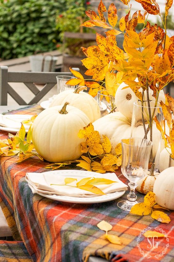 an all natural Thanksgiving tablescape with a bold plaid tablecloth, neutral porcelain, bold leaves and white pumpkins