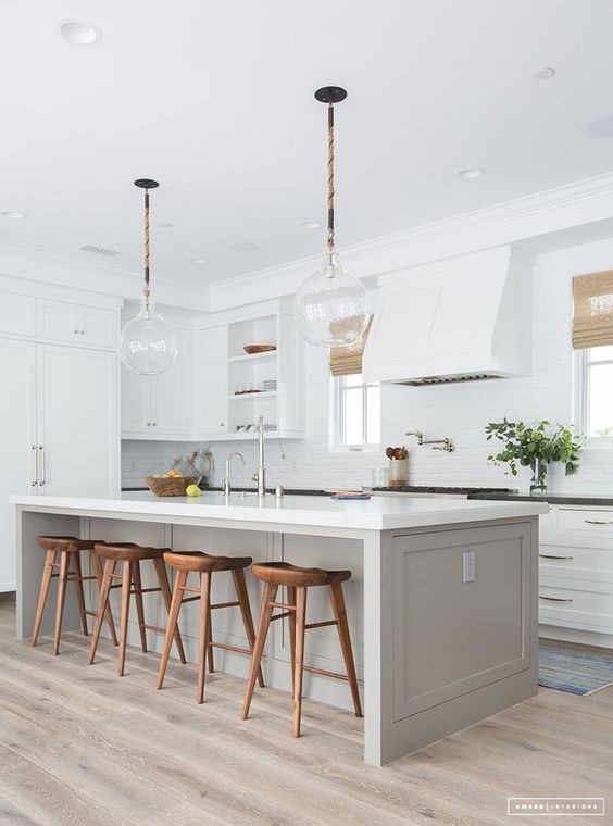 an elegant kitchen with white shaker style cabinets, black stone countertops, a dove grey kitchen island and rich-stained stools