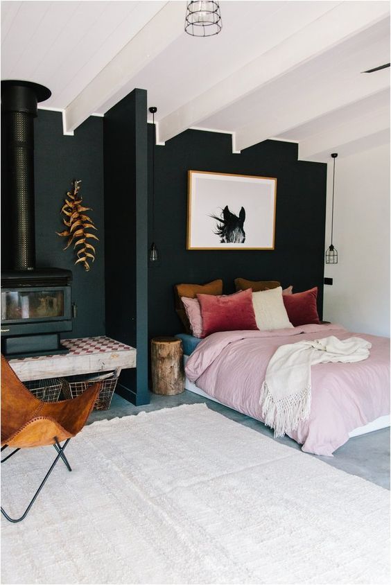 an eye-catchy bedroom with a black accent wall, a black hearth and a bed with pink and burgundy bedding, an amber chair