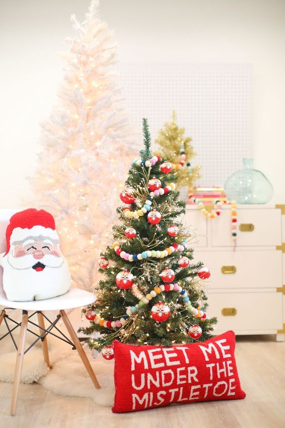 a Christmas tree with lights, colorful pompom garlands, a red pillow and a Santa one will add a fun and dreamy holiday feel