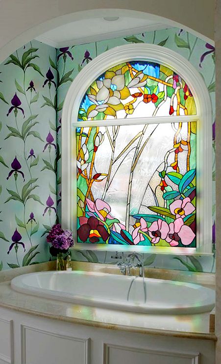 a bathroom with floral patterns on the walls and a gorgeous floral stained arched window over the tub, it keeps privacy of the space