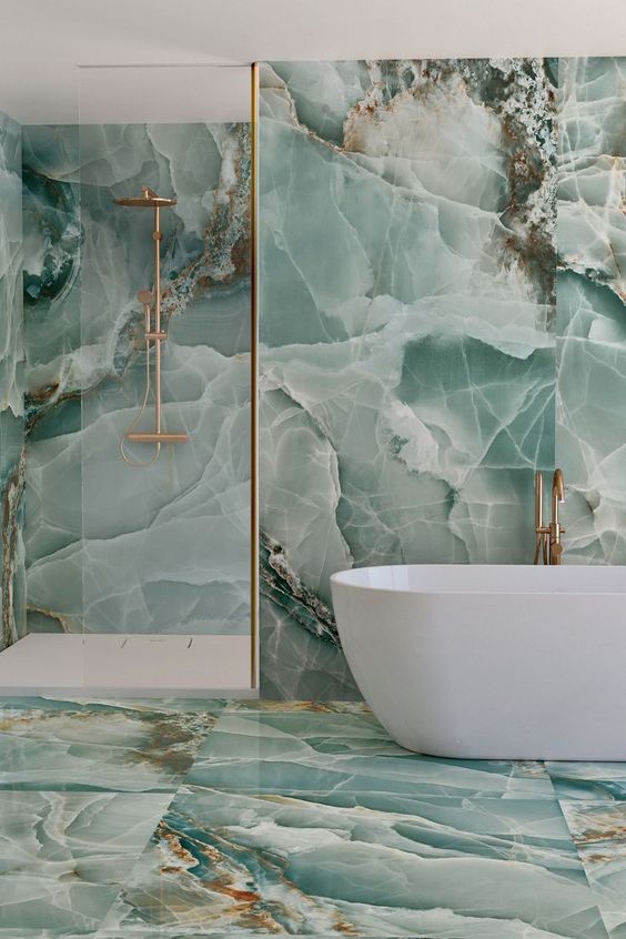 a beautiful bathroom clad with green ceramic tiles that imitate marble and onyx plus copper fixtures is amazing