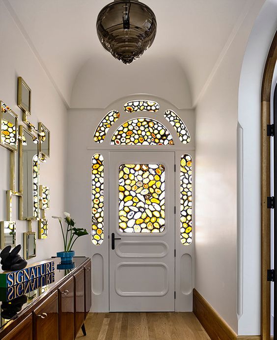 a catchy entryway with an arched door with stained glass and matching sidelights, a gallery wall of mirrors and a credenza