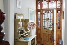 a chic vintage entryway with a tiled floor, a neutral storage unit, a pendant lamp and a door and sidelights with stained glass