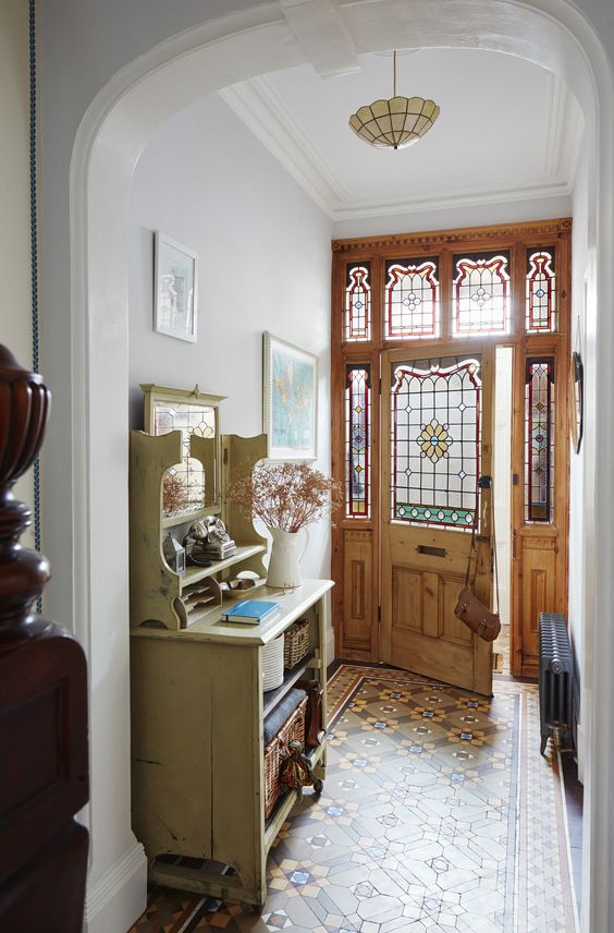 a chic vintage entryway with a tiled floor, a neutral storage unit, a pendant lamp and a door and sidelights with stained glass