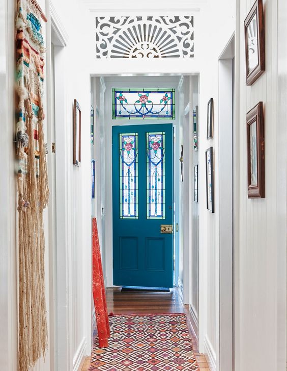 a colorful entryway with a blue door with stained glass and sidelights, a colorful printed rug and a bold macrame hanging