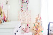 a colorful pompom garland, a Christmas tree with lights and bright ornaments and some tinsel trees on the dresser for a holiday feel