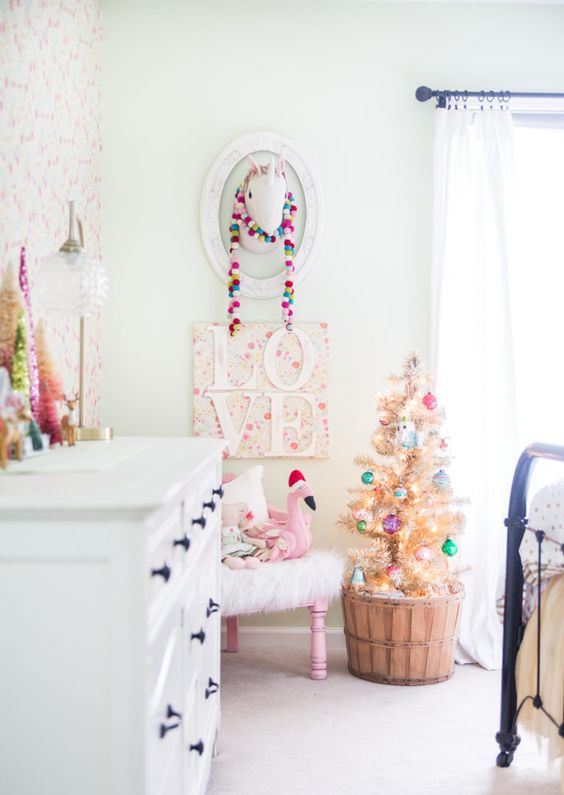 a colorful pompom garland, a Christmas tree with lights and bright ornaments and some tinsel trees on the dresser for a holiday feel