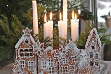 a creative candleholder of gingerbread houses with glazing and evergreens and tall and thin candles is amazing