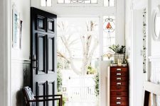 a lovely entryway with stained glass sidelights and a black door, a vintage bench, a fire cabinet and a dark chair with navy upholstery