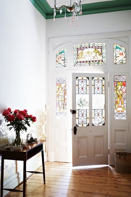 a pretty entry with a stained glass door and sidelights, with modern furntiure and a crystal chandelier plus bold blooms