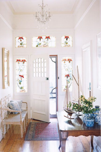 a pretty neutral entryway wiht sidelights with stained glass, a stained table, a vintage bench with blue printed pillows and a crystal chandelier