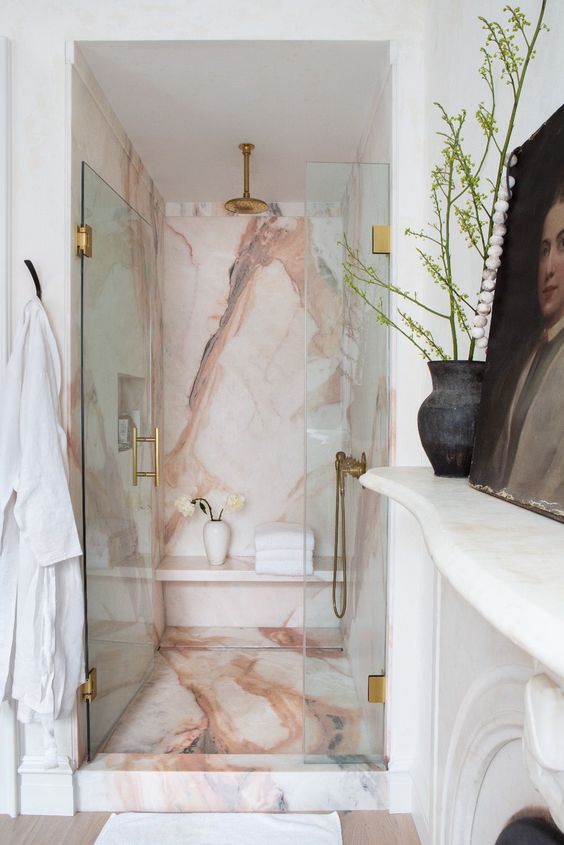 a refined bathroom with a shower space clad with pink onyx and a fireplace, a dark artwork and some greenery in a vase