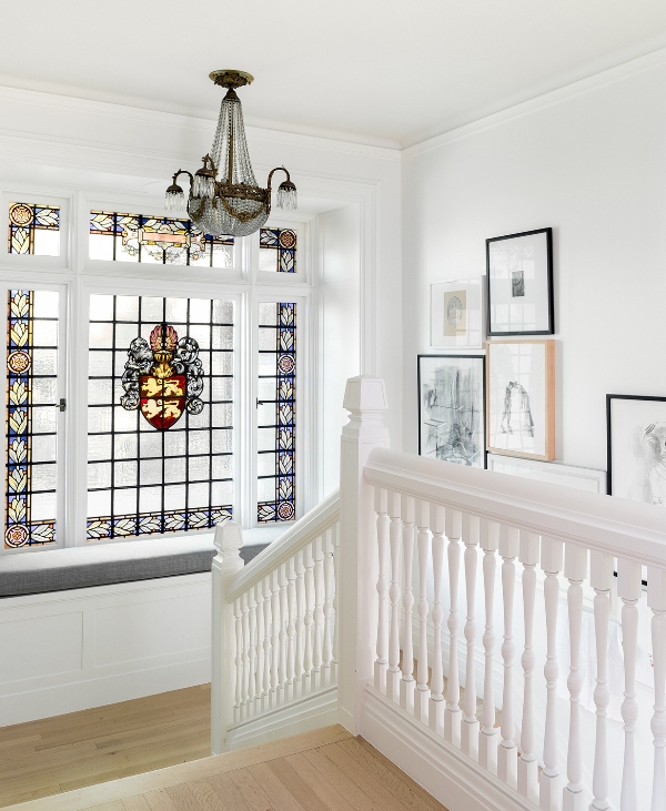 a staircase with a large window with stained glass and a built-in windowsill seating plus a gallery wall and a chic chandelier