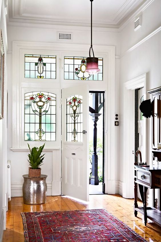 a stylish entryway with sidelights and a door with stained glass, a dark storage unit and a rack, a bold rug and a matching pendant lamp