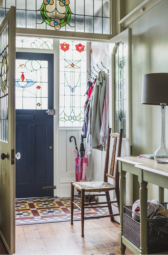 a stylish entryway with sidelights and the door with stained glass, a vintage green console table and a chair, a bold printed rug