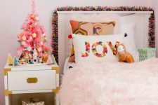 a tiny pink Christmas tree with colorful ornaments, a bright pompom garland and a printed pillow for holiday