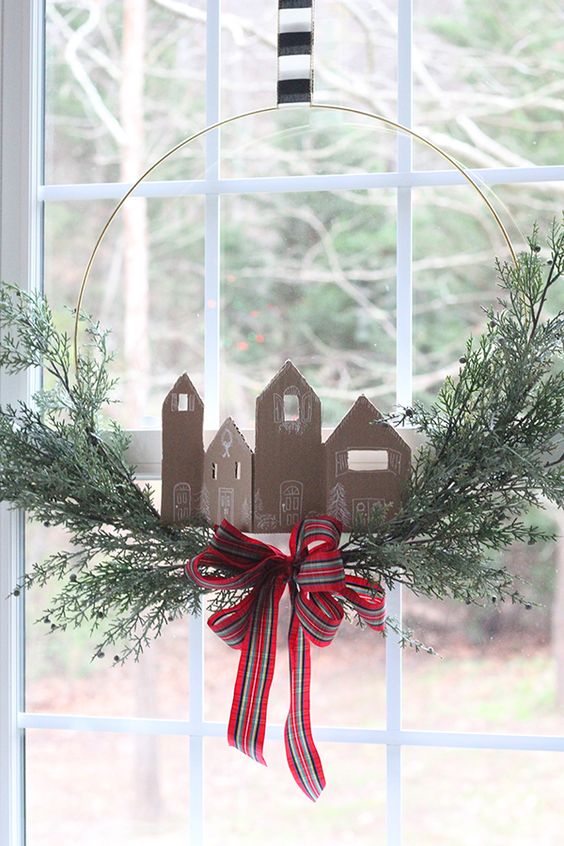 a wire wreath with greenery, cardboard houses imitating gingerbread ones and a plaid ribbon bow is a pretty idea for Christmas