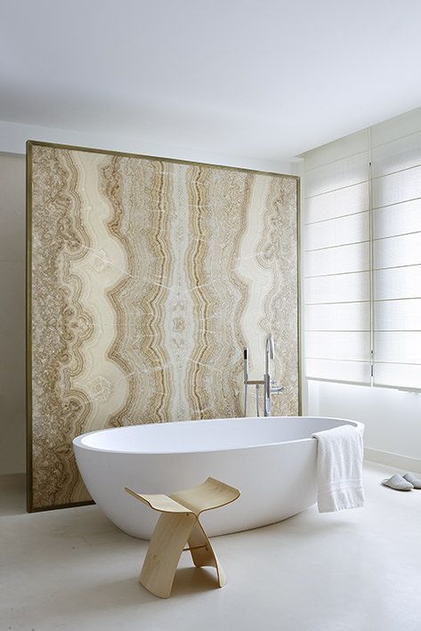 an organic bathroom in neutrals with an oval tub, a plywood stool and a beige onyx space divider that is a shower wall