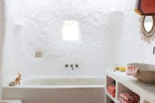 a boho bathroom with white walls, a stained ceiling with beams, a boho rug and a concrete vanity