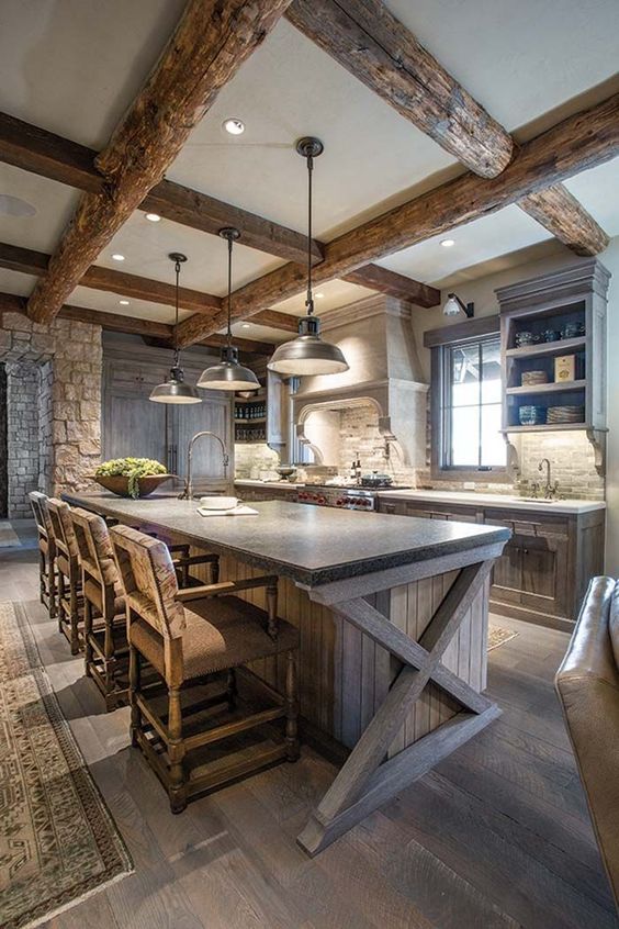 a chalet kitchen with rough wooden cabinetry and kitchen island, stone countertops, wooden beams and pendant lamps and vintage stools