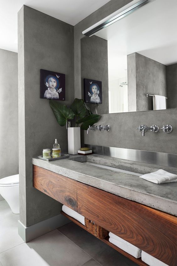 a concrete bathroom with a concrete vanity and wooden storage units, a large mirror and a window to enjoy natural light