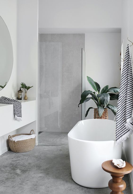 a contemporary bathroom with concrete walls and a floor, a white vanity and an oval tub, baskets and woven planters