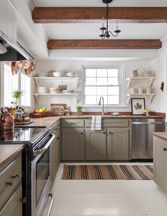 a cozy modern farmhouse kitchen with green cabinetry, wooden countertops and wooden beams that match and warm up the space