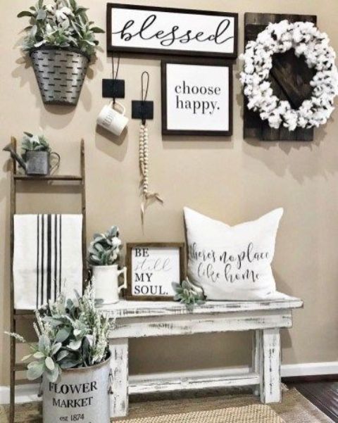 a farmhouse entryway with a monochromatic gallery wall, a whitewashed bench and some greenery arrangements