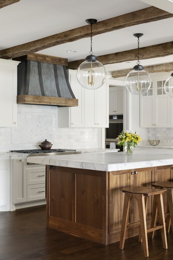a farmhouse kitchen in neutrals, with a wooden kitchen island and stools and wooden beams that cozy up the space