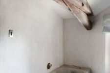a minimalist bathroom with white walls, a concrete tub and rich stained wooden beams for a softer and warmer look