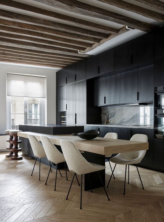 a minimalist kitchen with black cabinets, a marble backsplash, a two-part kitchen island and rough wooden beams