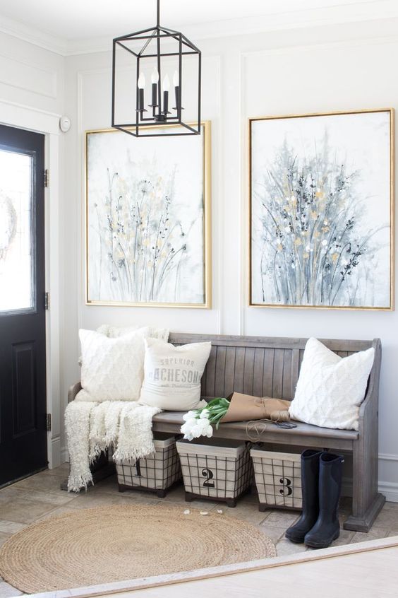 a modern farmhouse entryway with a weathered wood bench, wire baskets for storage, neutral pillows and artworks