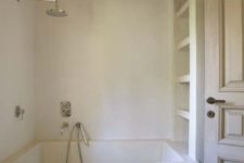 a neutral bathroom with white walls, a shower space, a storage unit and wooden beams to soften the space