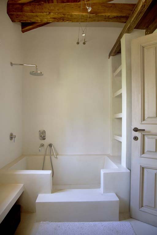 a neutral bathroom with white walls, a shower space, a storage unit and wooden beams to soften the space