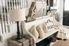 a neutral farmhouse entryway with a large and creative gallery wall, a white bench, neutral pillows and blankets plus a woven box
