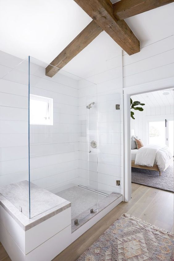 a neutral modern farmhouse bathroom clad with white wood, with dark stained beams and neutral tiles