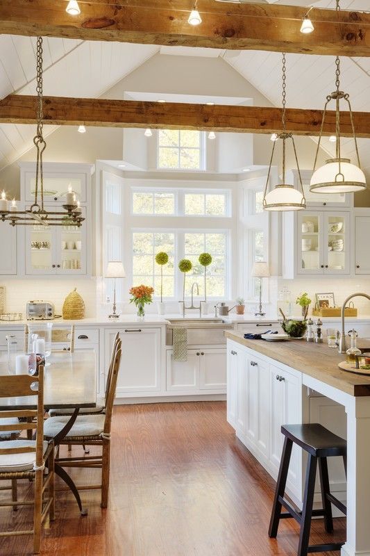 a neutral modern farmhouse kitchen with light-colored wooden beams, wooden chairs and countertops that soften the look