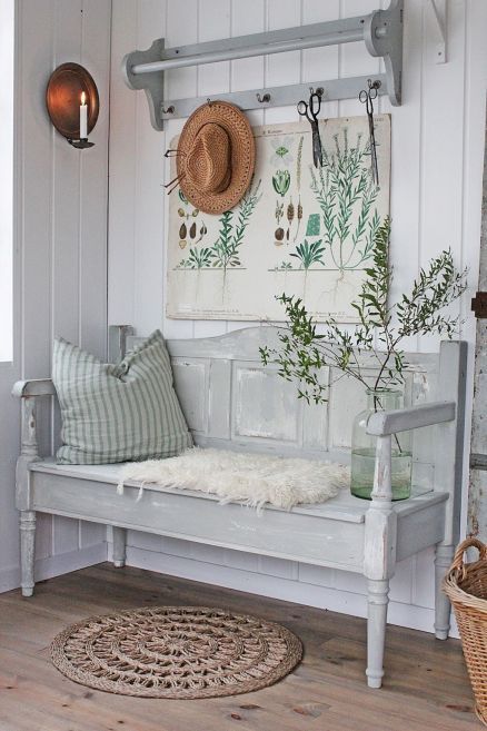 a neutral vintage farmhouse entryway with a grey bench, a vintage poster as an artwork, a rack and a pillow