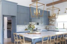 a refined blue kitchen with white surfaces, wooden beams, wooden chairs and brass chandeliers is stylish and chic