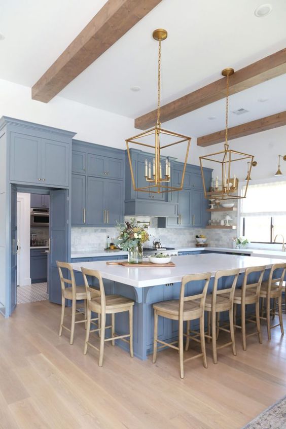 a refined blue kitchen with white surfaces, wooden beams, wooden chairs and brass chandeliers is stylish and chic