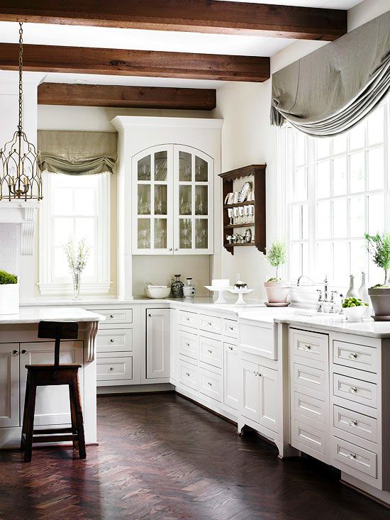 a vintage white kitchen with elegant cabinetry, dark wooden beams and sotols that add interest, grey and green curtains