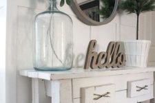 a white console table, baskets for storage, a round mirror in a wooden frame and some greenery in a bottle