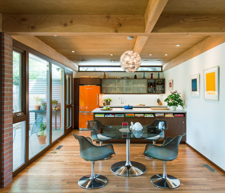 a mid-century modern kitchen with a large wooden kitchen island, an orange fridge, a dining zone with comfy chairs  (Architectural Workshop)