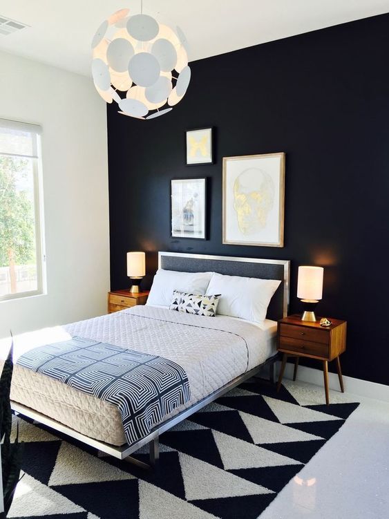 a bold and dramatic mid-century modern bedroom with a blakc statement wall, a geometric rug, a black bed and rich-stained nightstands