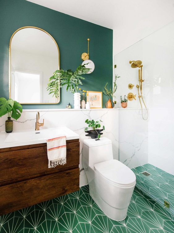 a bright mid-century modern bathroom with a teal wall, an emerald print tile floor, a stained vanity and touches of gold