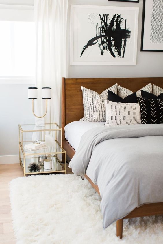 a bright mid-century modern bedroom with a rich stained bed, a white fluffy rug, a gilded frame nightstand and an abstract artwork