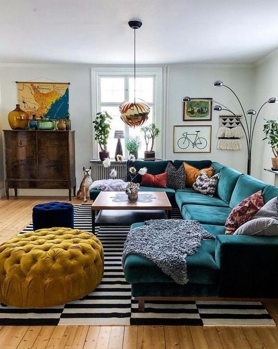a bright mid-century modern living room with a stained storage unit, a dark green sectional, a yellow ottoman and a navy pouf, colorful pillows and a bold gallery wall